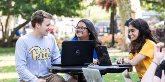 Three students sit at a laptop and share a conversation.